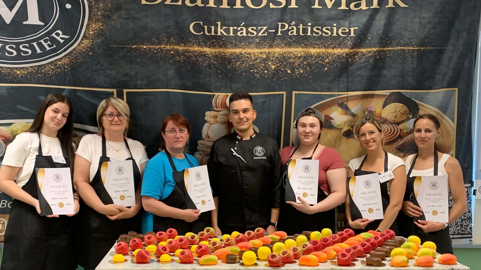 Workshop-csoport oklevéllel Szamosi Márkkal, előttük a saját készítésű édességek